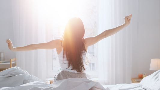 Waking woman backlit by sun through a sheer curtain.